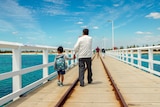 A man and a child walk along a long wooden jetty.