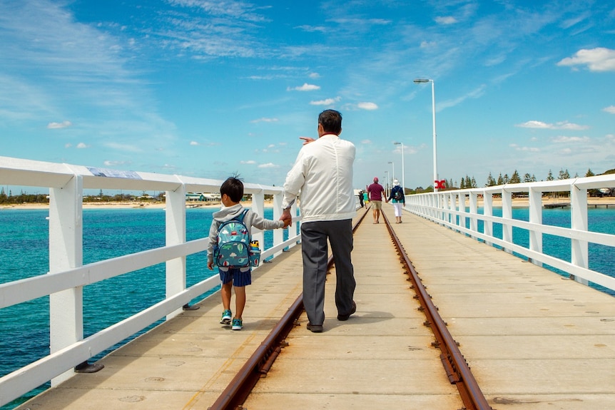 A man and his grandchild walk along a long wooden jetty.