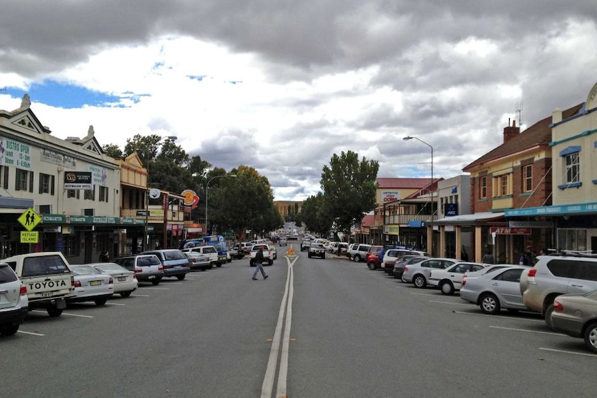 The main street of a country town, lined by cars.