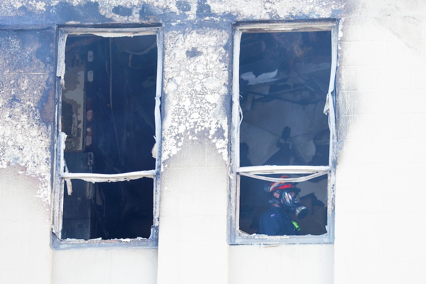 A firefighter is seen through one of two scorched windows 