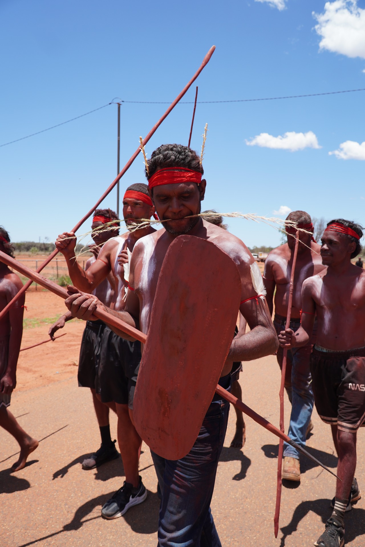 Aboriginal men wearing red headband and spears and sheild stand together 