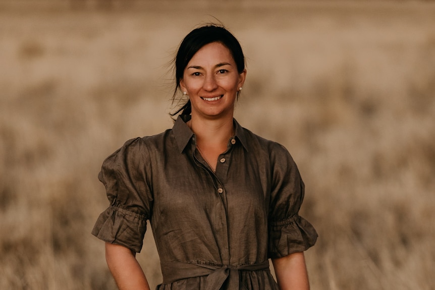 A woman with pear earrings and stylish dark dress smiles.