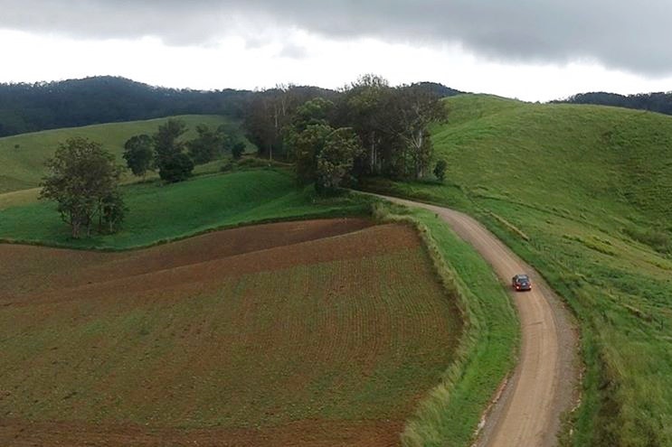 Aerial shot of rolling hills and a car driving down a country road.