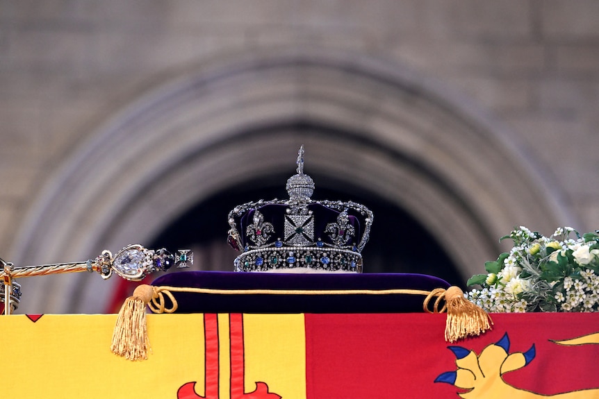 An ornate crown rests on top of a purple pillow placed on top of a coffin.