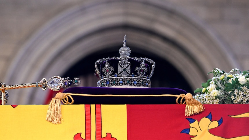 An ornate crown rests on top of a purple pillow placed on top of a coffin.