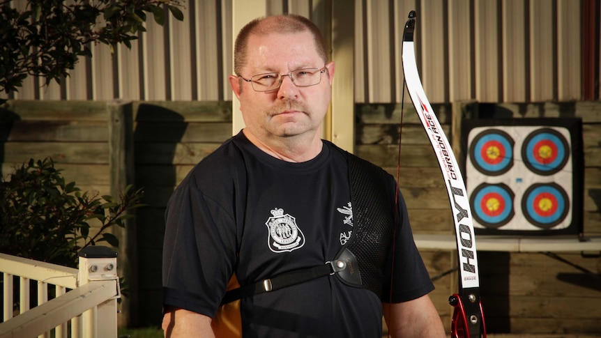 A man with an archery bow standing at a short distance from a target in his backyard.