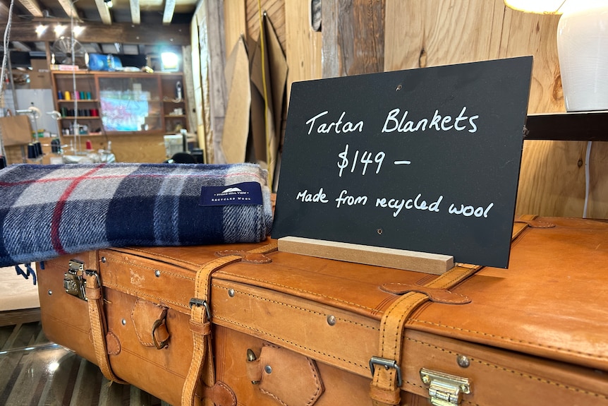A tartan blanket sits on an antique suitcase, along with a sign indicating the blanket's price to be $149.