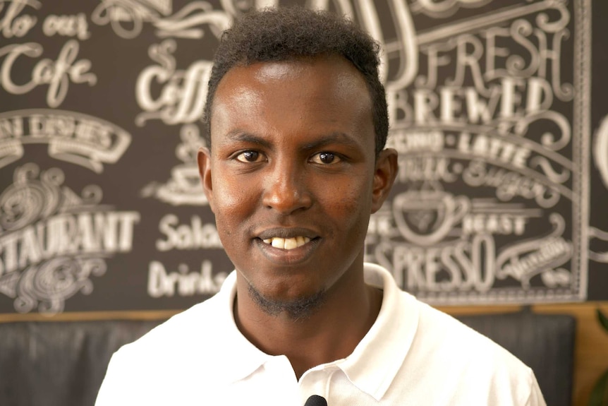 A young, Somalin-born man smiles for a photo.