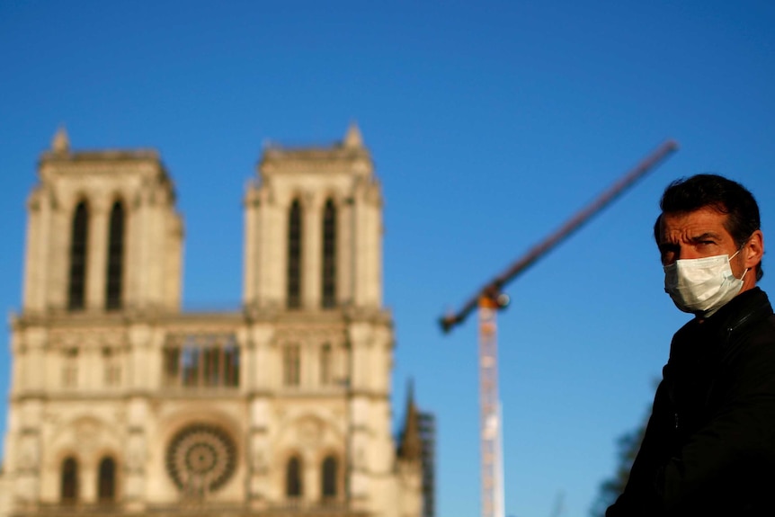 A man wearing a face mask listens to the Notre-Dame de Paris Cathedral's great bell ringing.