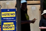 A sign that reads "Vote no, Don't know" outside a polling booth with volunteers handing out yes brochures