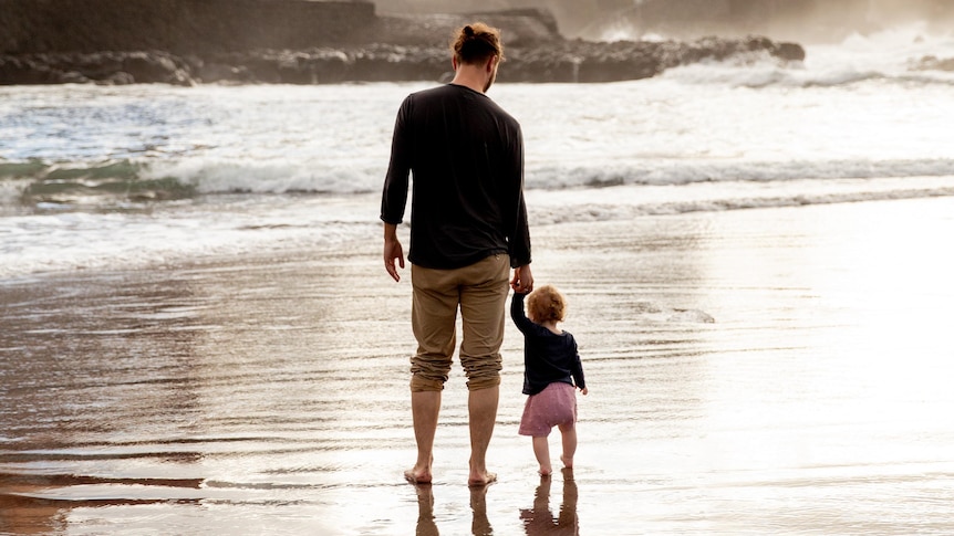 A man and young child walk along the waters edge.