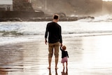 A man and young child walk along the waters edge.