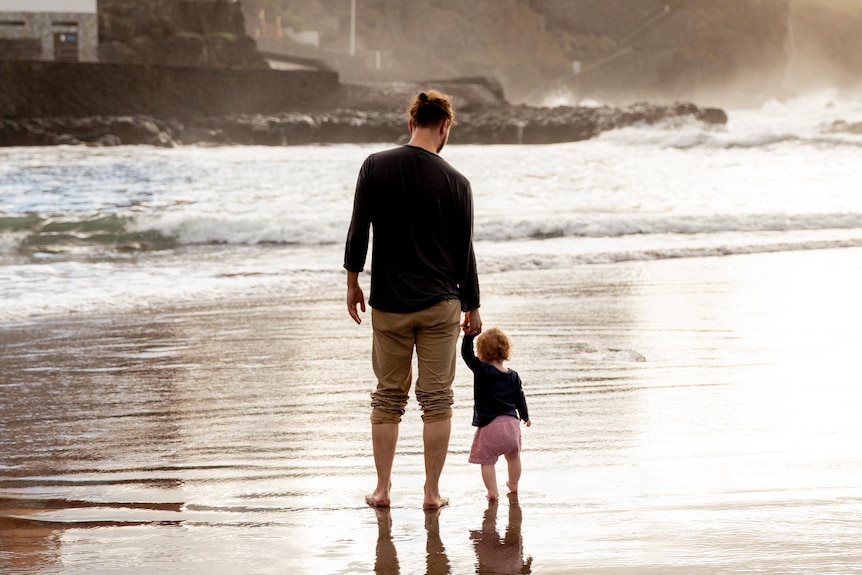 A man and young child walk along the waters edge.
