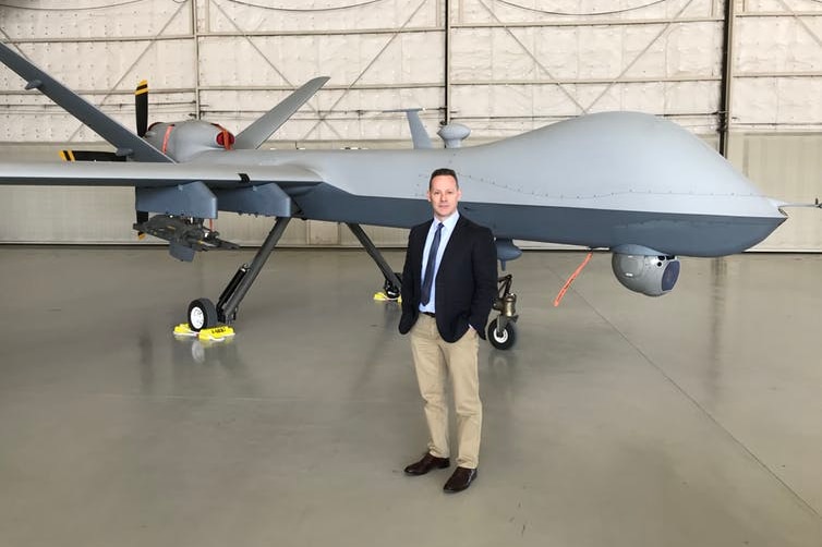 Dr Peter Lee stands next to an MQ Reaper drone.