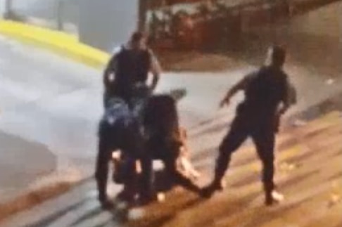 A grainy image showing four police restraining a person on a street at night.