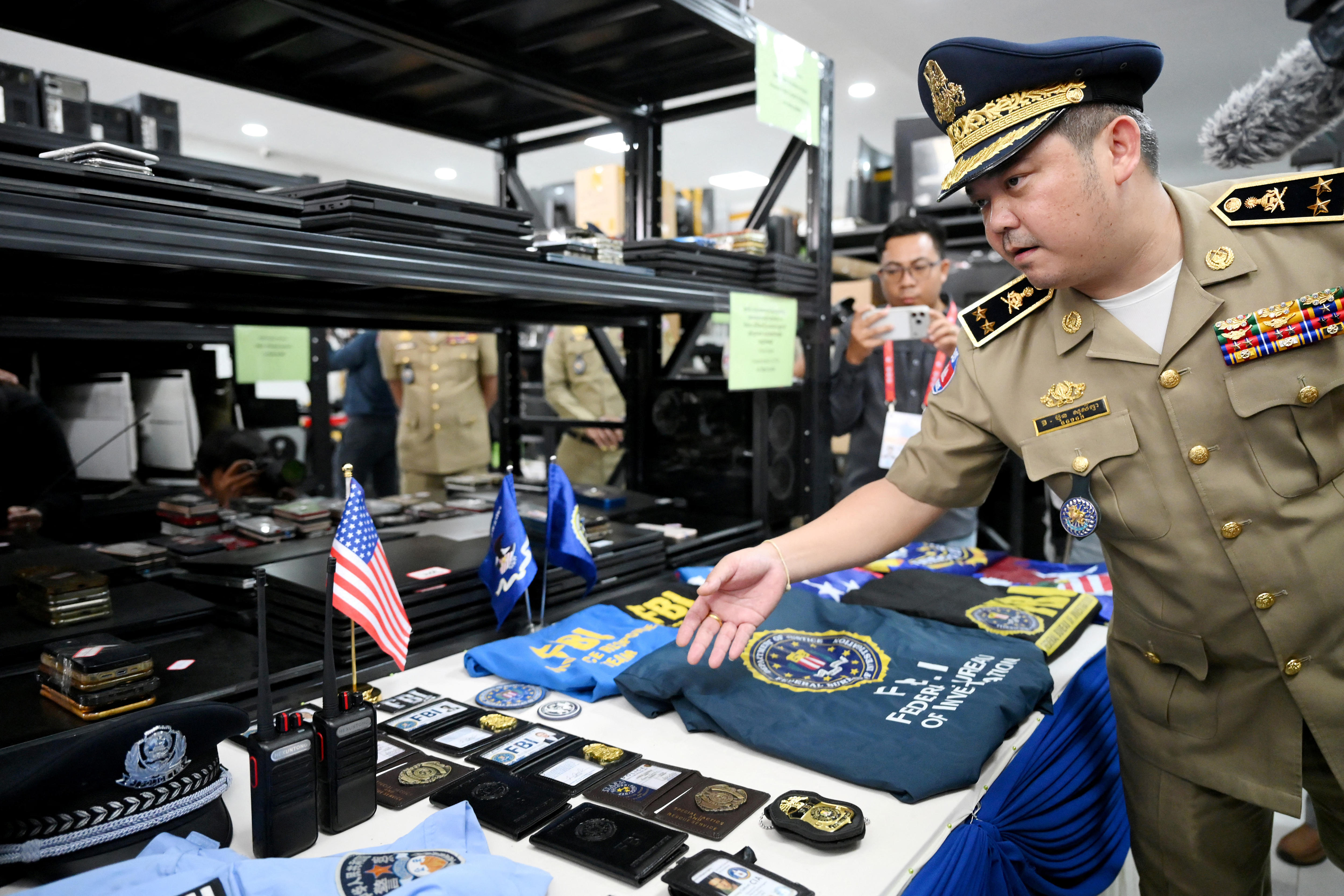 A Cambodian police officer points to fake law enforcement items laid out on a table.