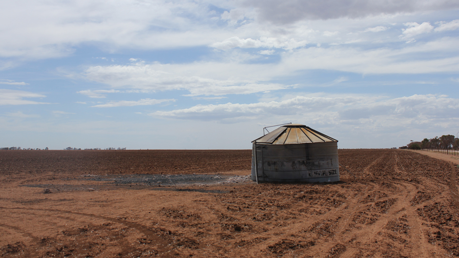 A grain bin with ash and burnt soil in front of it standing in a bare field of red dirt.