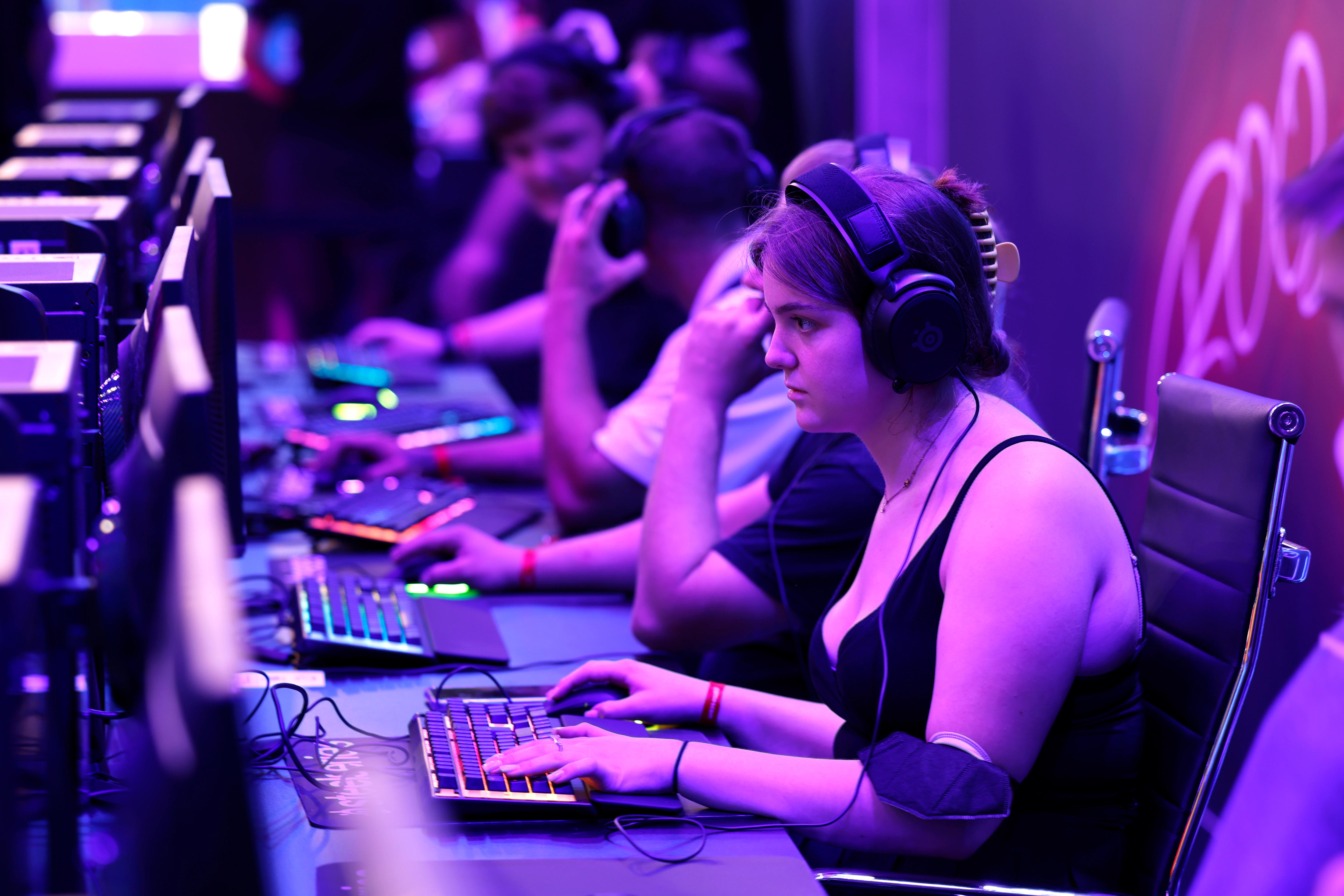 A purple-blue backlit desk featuring multiple people playing games on keyboards. 
