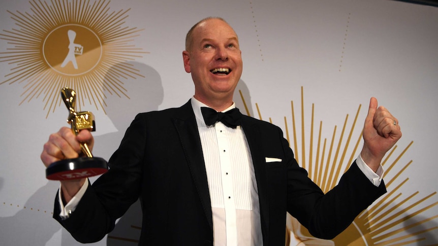 Tom Gleeson, wearing a tuxedo, clenches his left fist while his right hand holds the Gold Logie award.