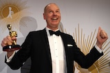 Tom Gleeson, wearing a tuxedo, clenches his left fist while his right hand holds the Gold Logie award.