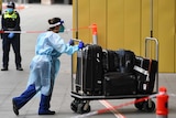 A healthcare worker in full PPE pushes luggage into a hotel.