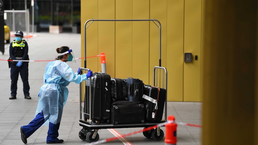 A healthcare worker in full PPE pushes luggage into a hotel.