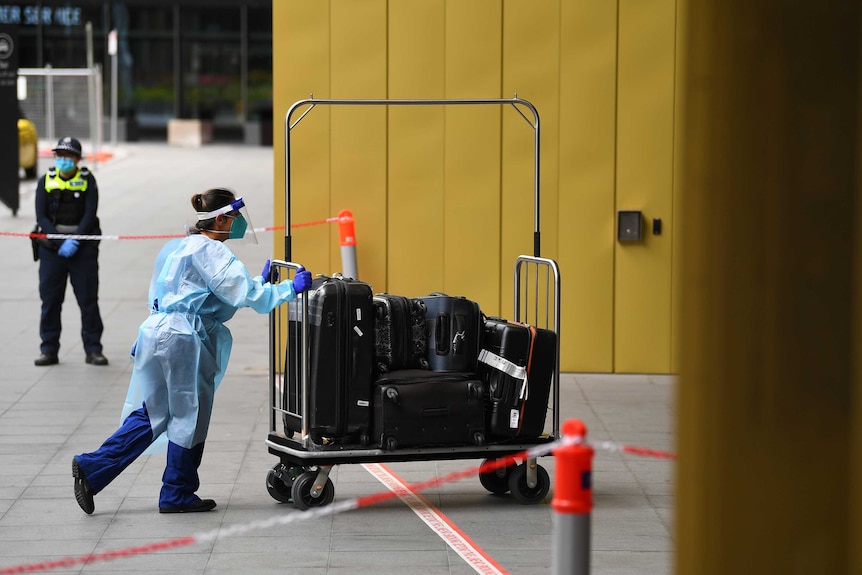 A healthcare worker in full PPE pushes luggage into a hotel.