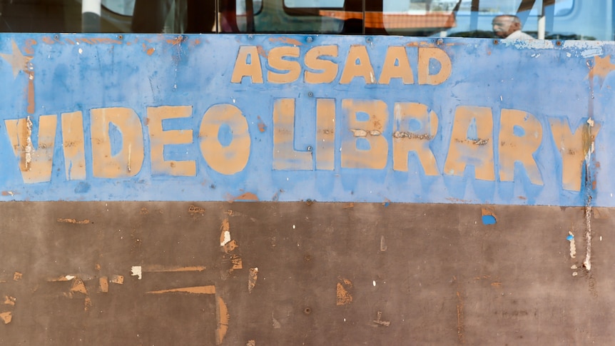 an old blue and brown hand-painted sign saying: Assaad video library