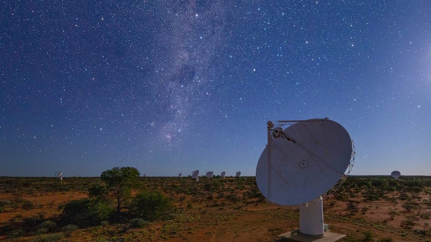 A dark blue sky at night filled with dazzling stars. Dish-shaped antennas are scattered across a vast red dust field.