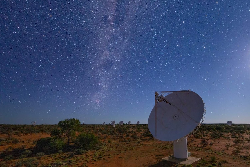 A dark blue sky at night filled with dazzling stars. Dish-shaped antennas are scattered across a vast red dust field.