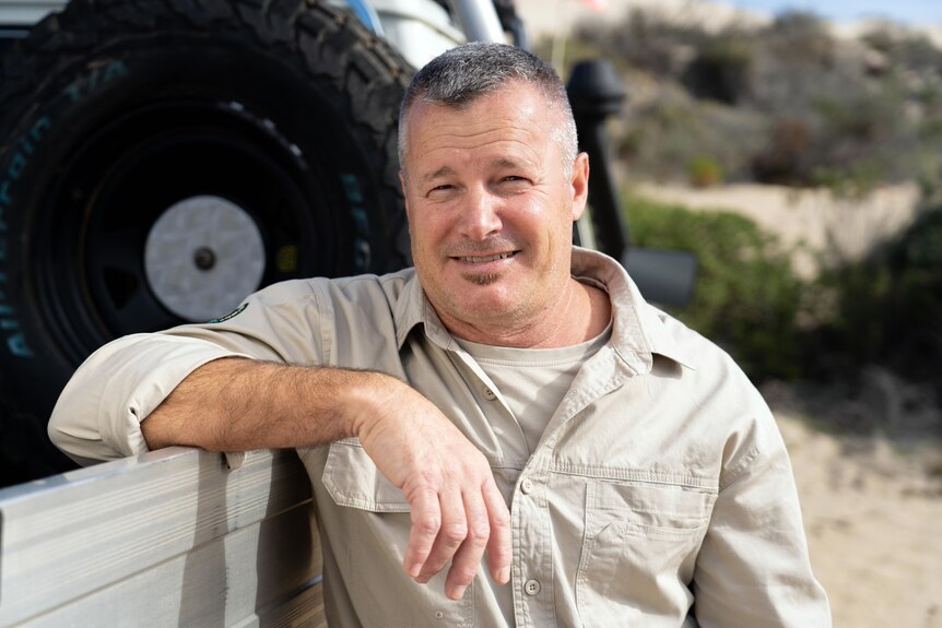 A man resting his forearm against a ute smiles at the camera.