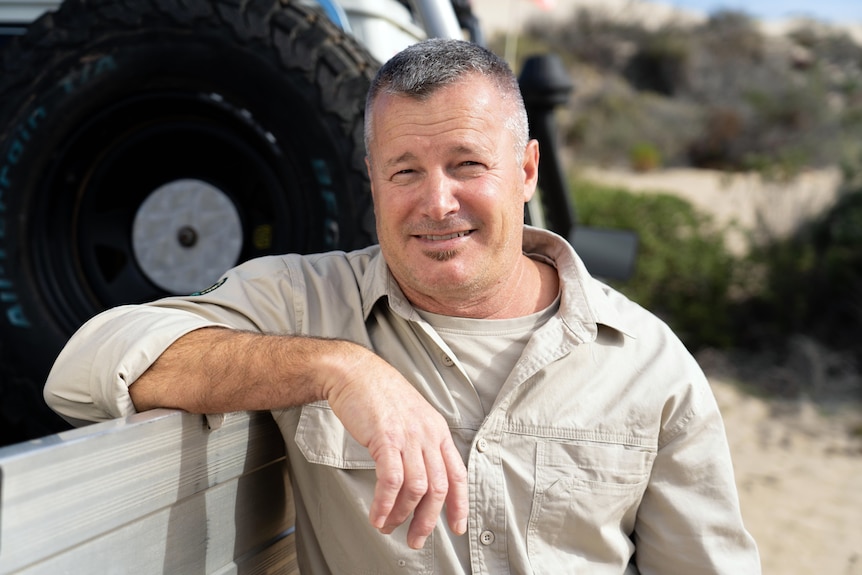 A man resting his forearm against a ute smiles at the camera.