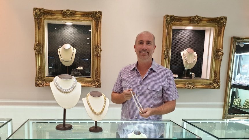 A man in a jewellery store holds up a pearl necklace