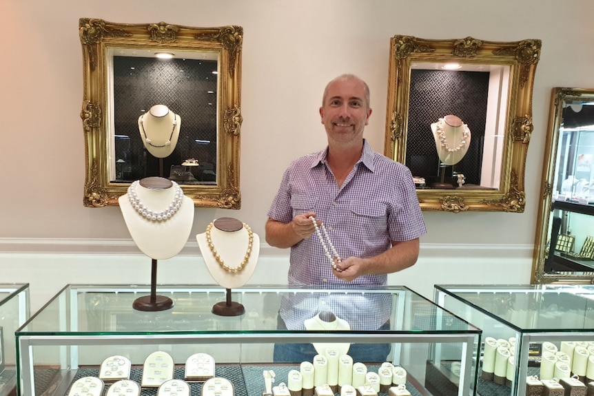 A man in a jewellery store holds up a pearl necklace
