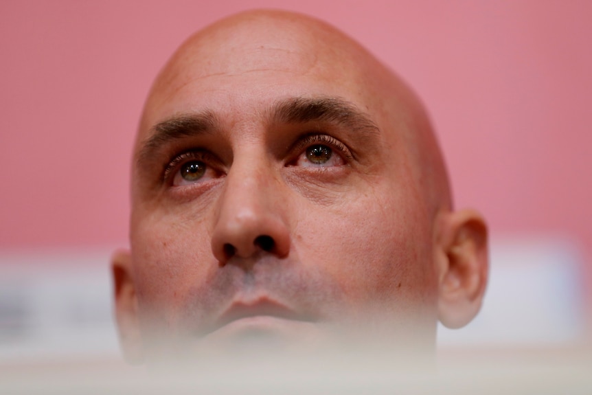 Luis Rubiales, a bald man, looks over the top and beyond the frame of the image. 