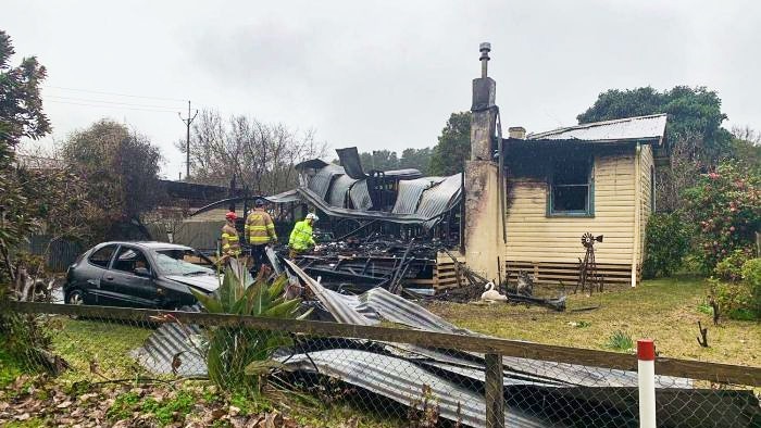 A blackened house with a collapsed roof and a car