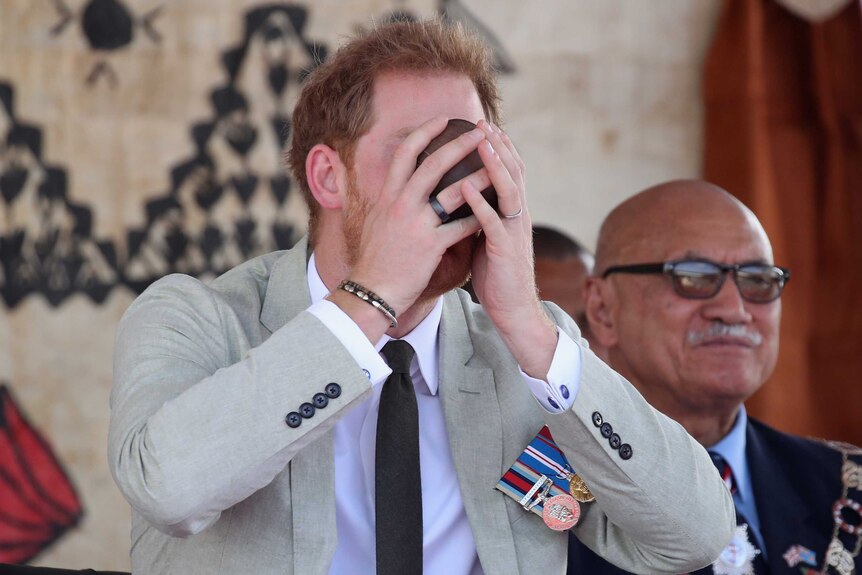 Prince Harry cups a coconut cup to his face and slurps kava.