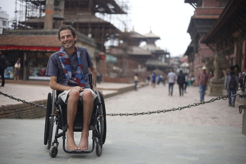 A man in a wheelchair smiling in front of temples in Nepal
