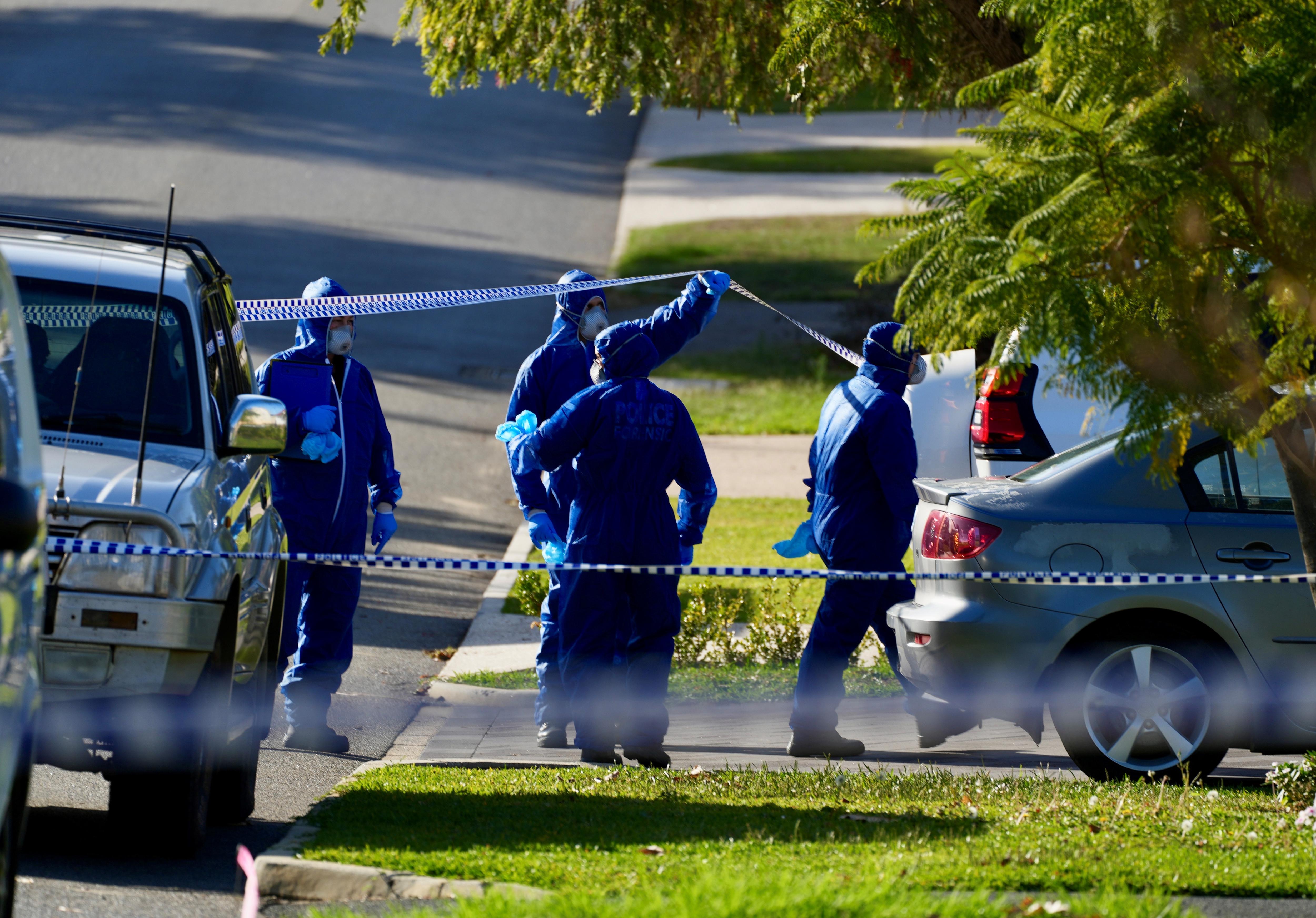 A group of forensics police officers wearing blue overalls outside a home on a suburban street.
