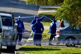 A group of forensics police officers wearing blue overalls outside a home on a suburban street.