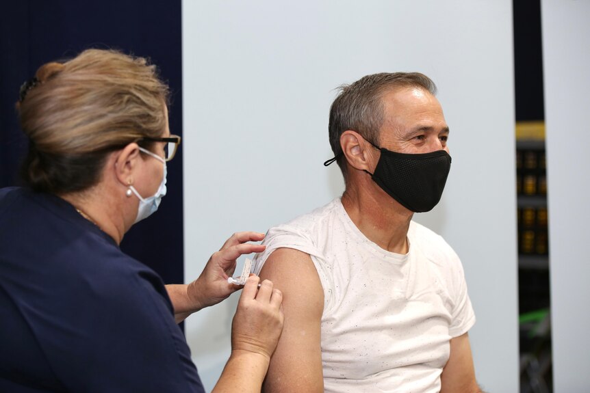 Health Minister Roger Cook getting an injection while wearing a mask.