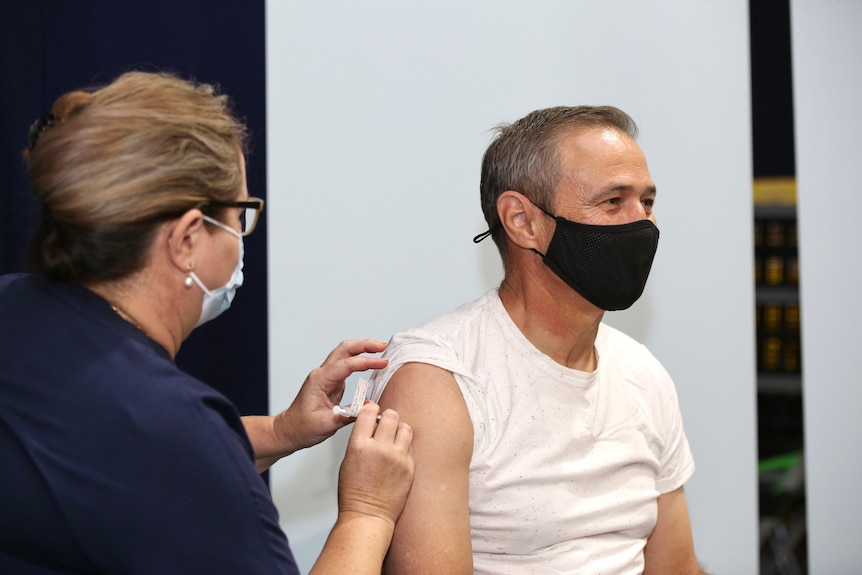 Health Minister Roger Cook receives an injection while wearing a mask.