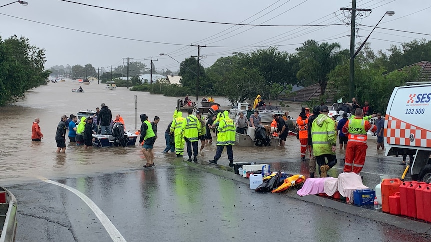 people in small boats on a flooded street as other people wait to help them