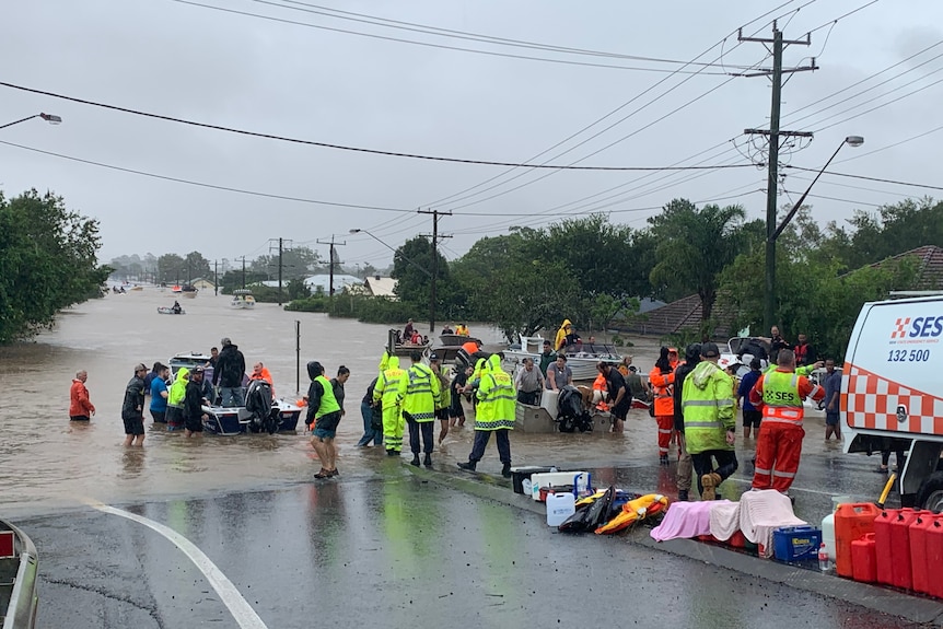 people in small boats on a flooded street as other people wait to help them