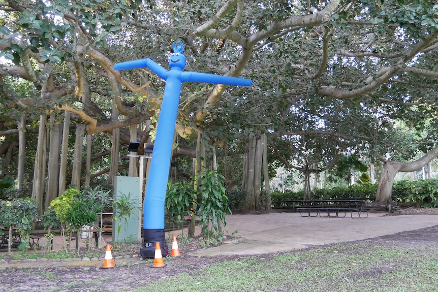 A blue inflatable wavy figure standing in the middle of old trees
