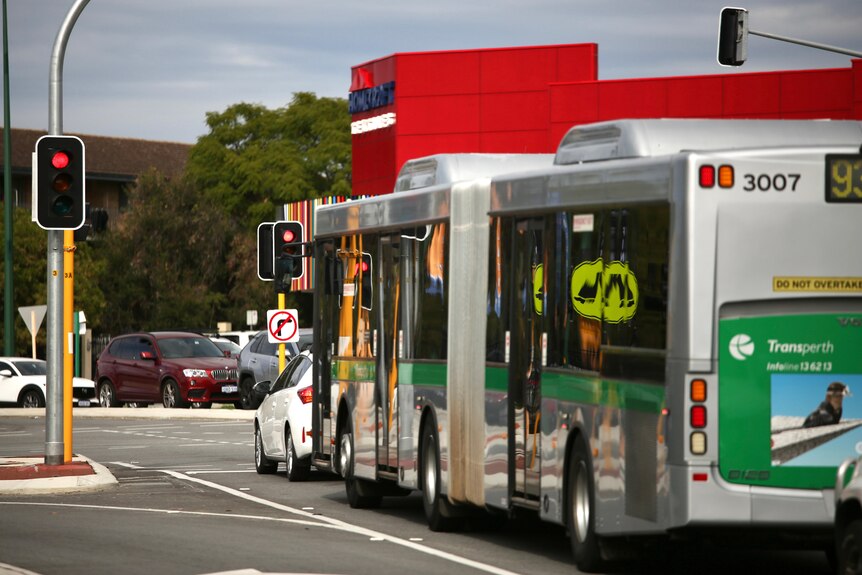 A bus waits behind a white car at a red light at the intersection of Albany Highway with Shepperton and Welshpool Roads.
