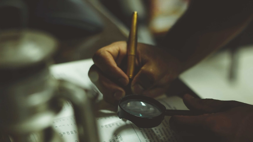 Person writing in book and holding a magnifying glass