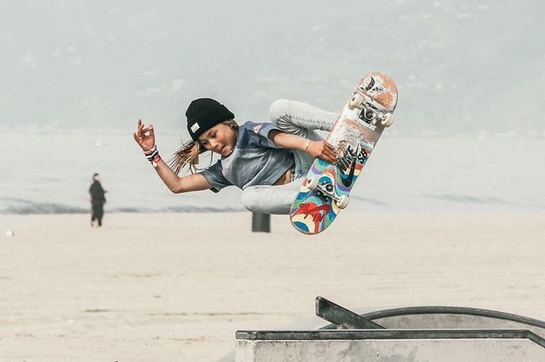 Sky Brown in the air holding a skateboard.