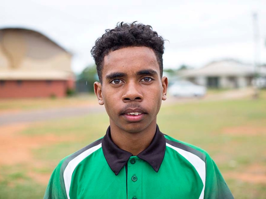 Young 14-year-old boy looks directly at the camera, wearing a green and black t-shirt