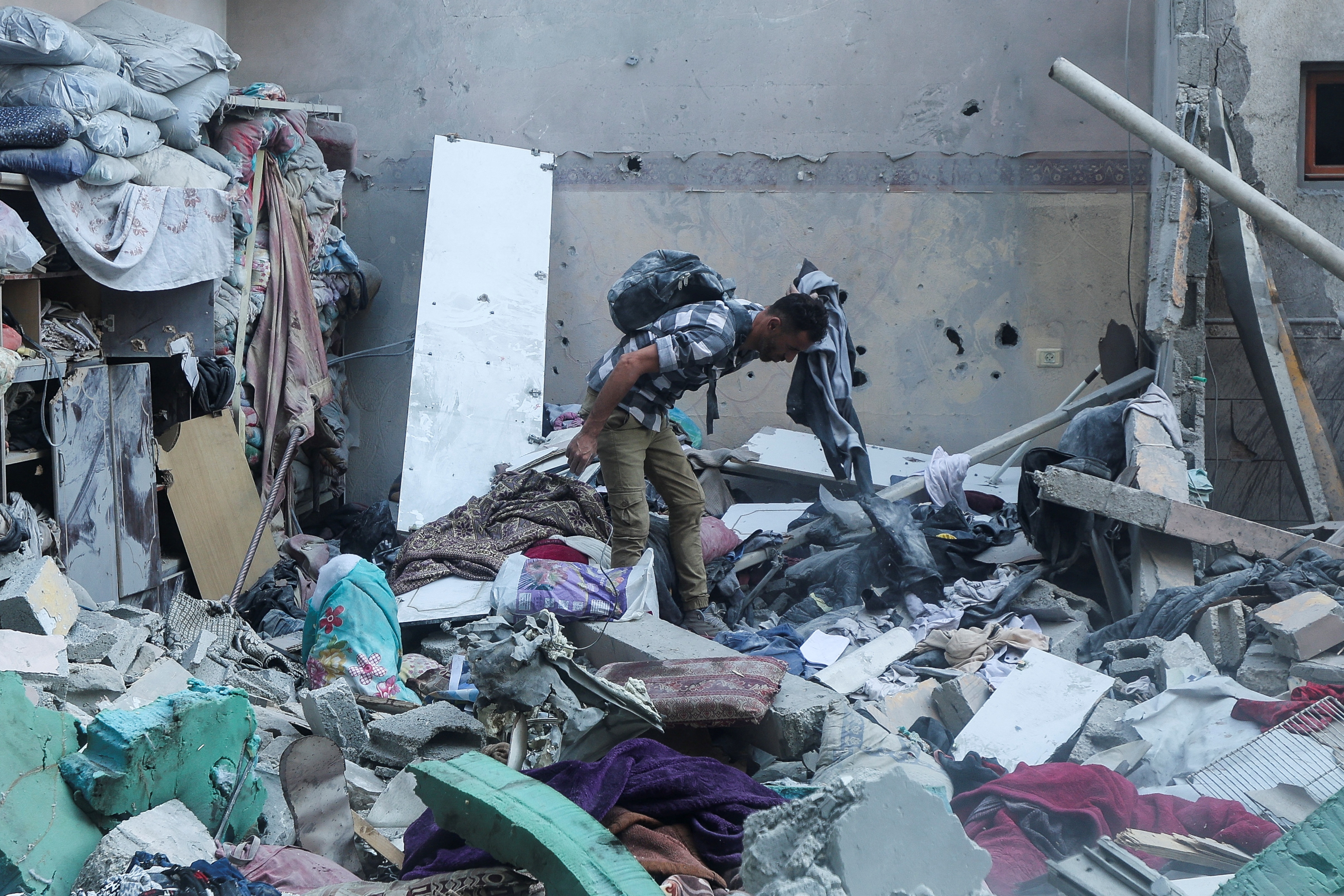A man stands among the rubble of a house, looking down